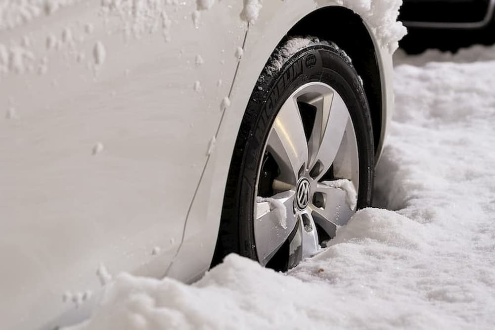 Coche blanco con neumatico hundido en la nieve alta