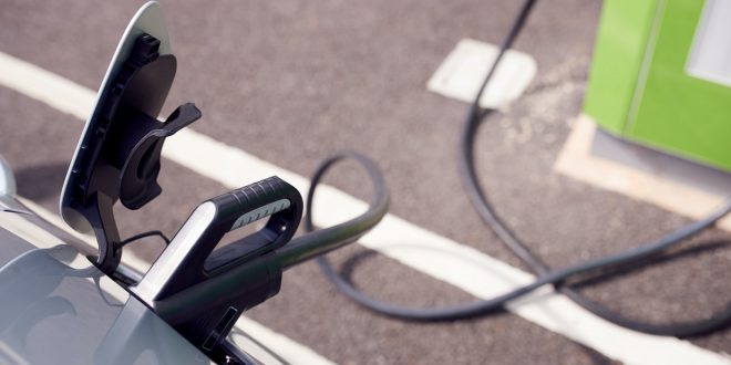 Close Up Of Power Cable Charging Electric Car Outdoors In Supermarket Car Park