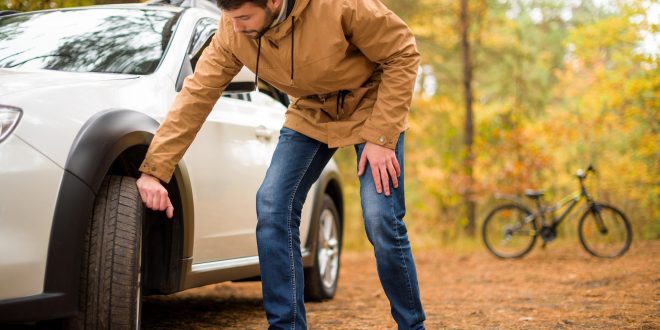 Young bearded man checking car tyre in autumn forest