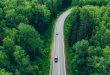 Aerial view of curved country road with cars and green summer woods.