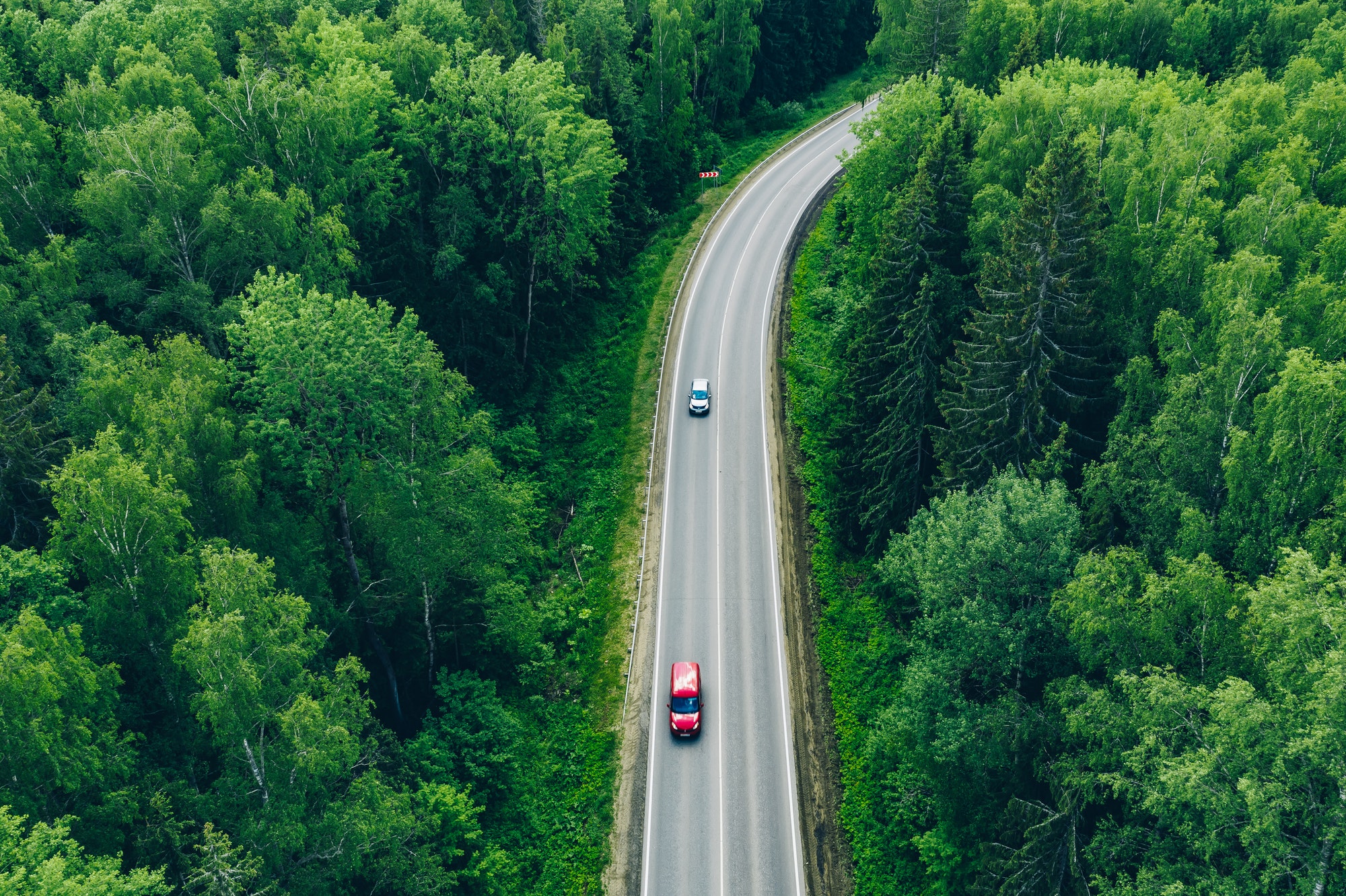 Aerial view of curved country road with cars and green summer woods.