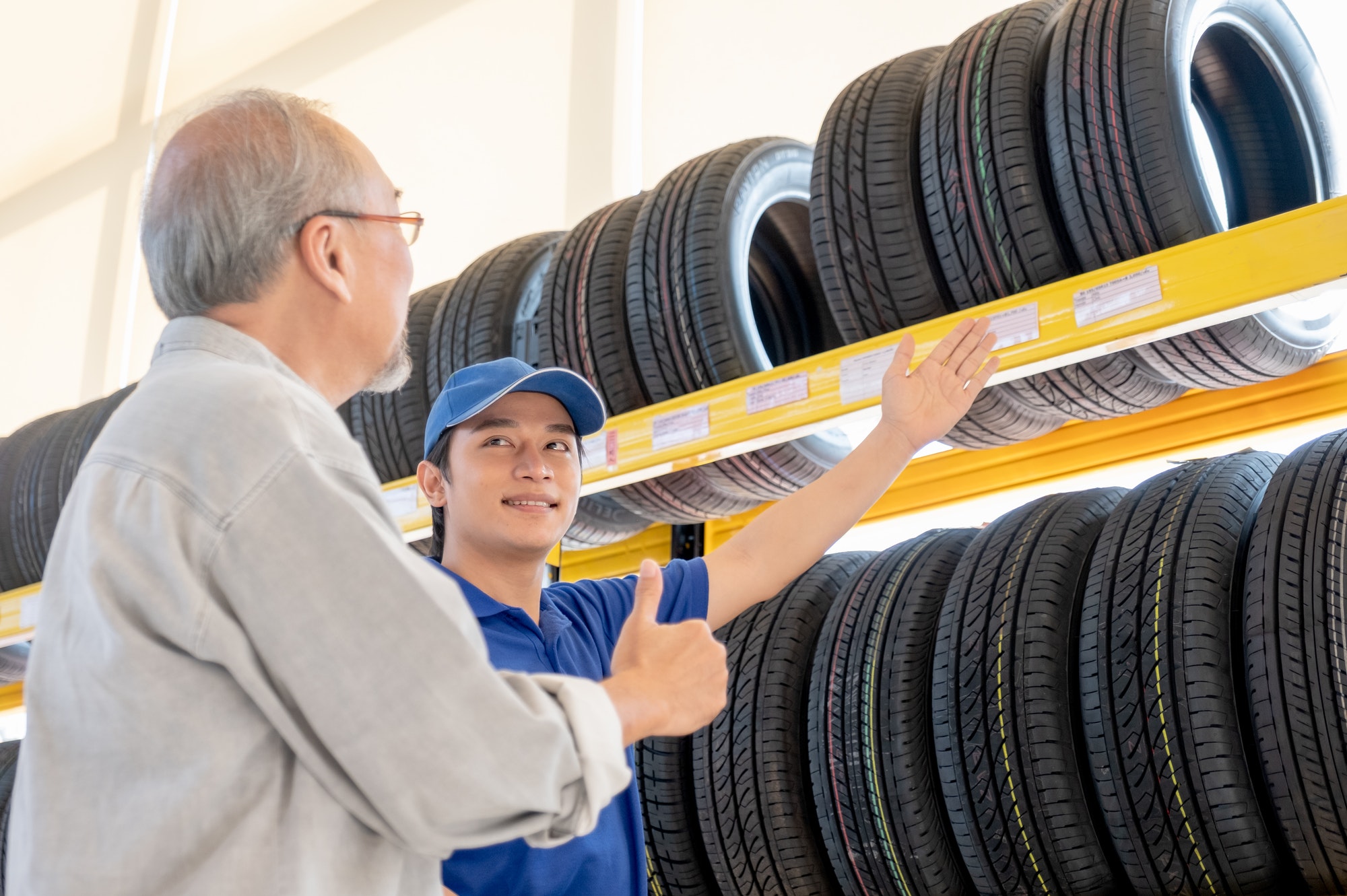 Asian worker of auto parts shop explain and suggest good quality tire to senior customer