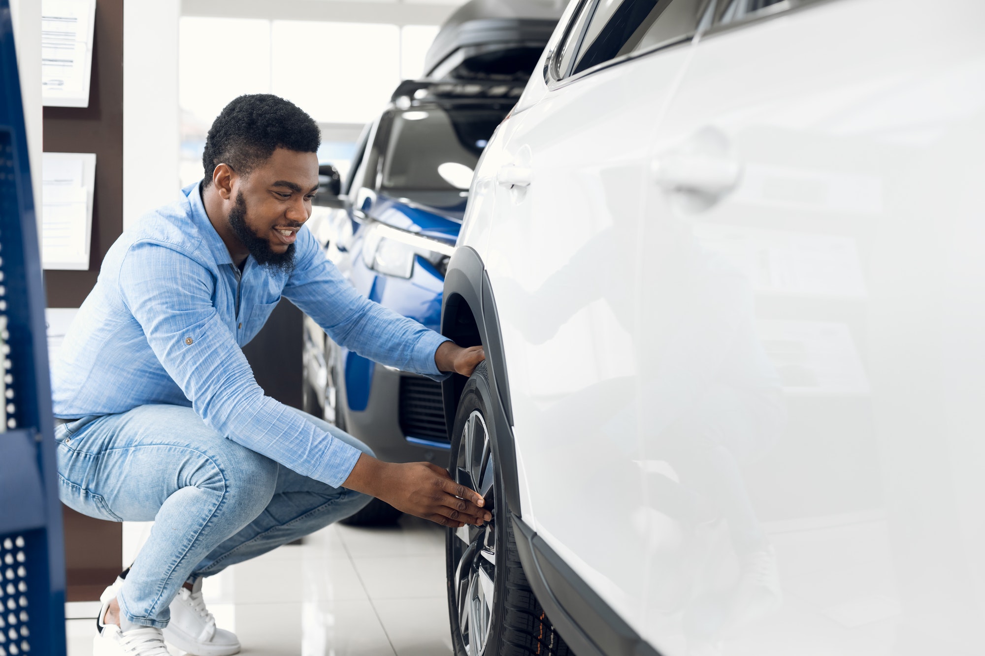 Black Guy Checking Car Wheels And Tyres In Dealership Showroom