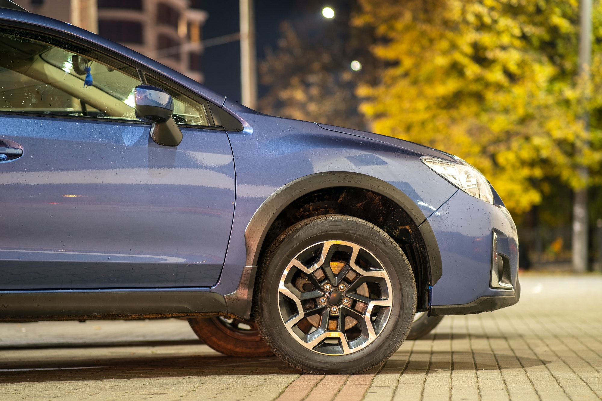 Blue car parked on brightly illuminated city street at night