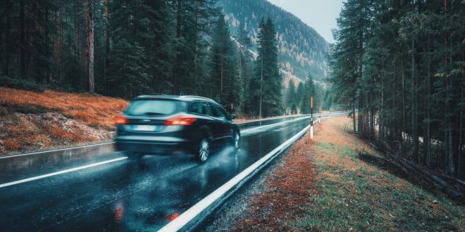 Blurred car in motion on the road in autumn forest in rain