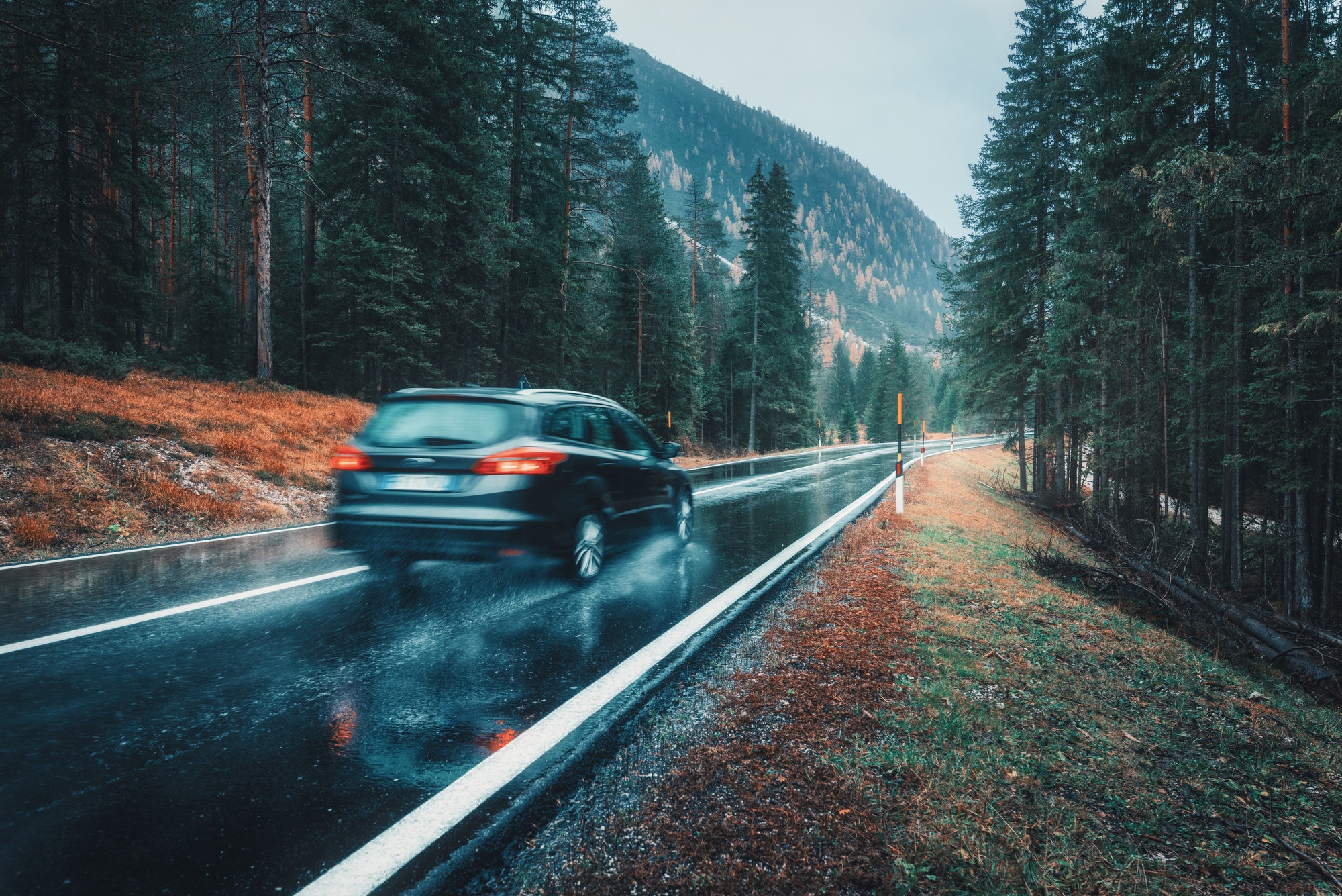 Blurred car in motion on the road in autumn forest in rain
