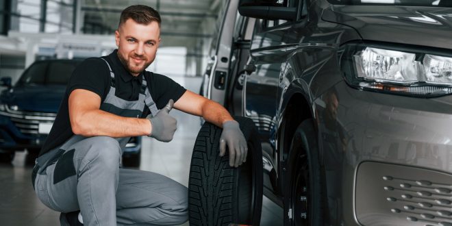 Changing of the tires. Man in uniform is working in the autosalon at daytime