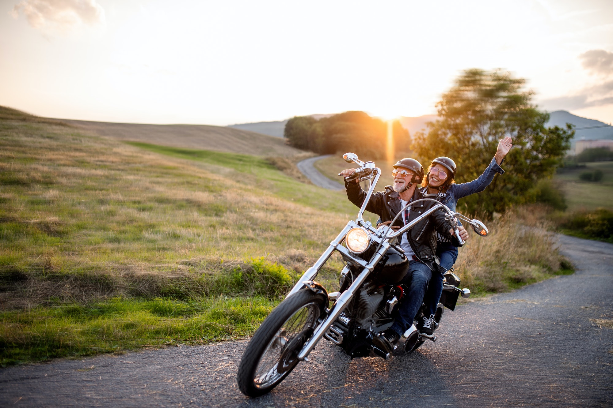 Cheerful senior couple travellers with motorbike in countryside.