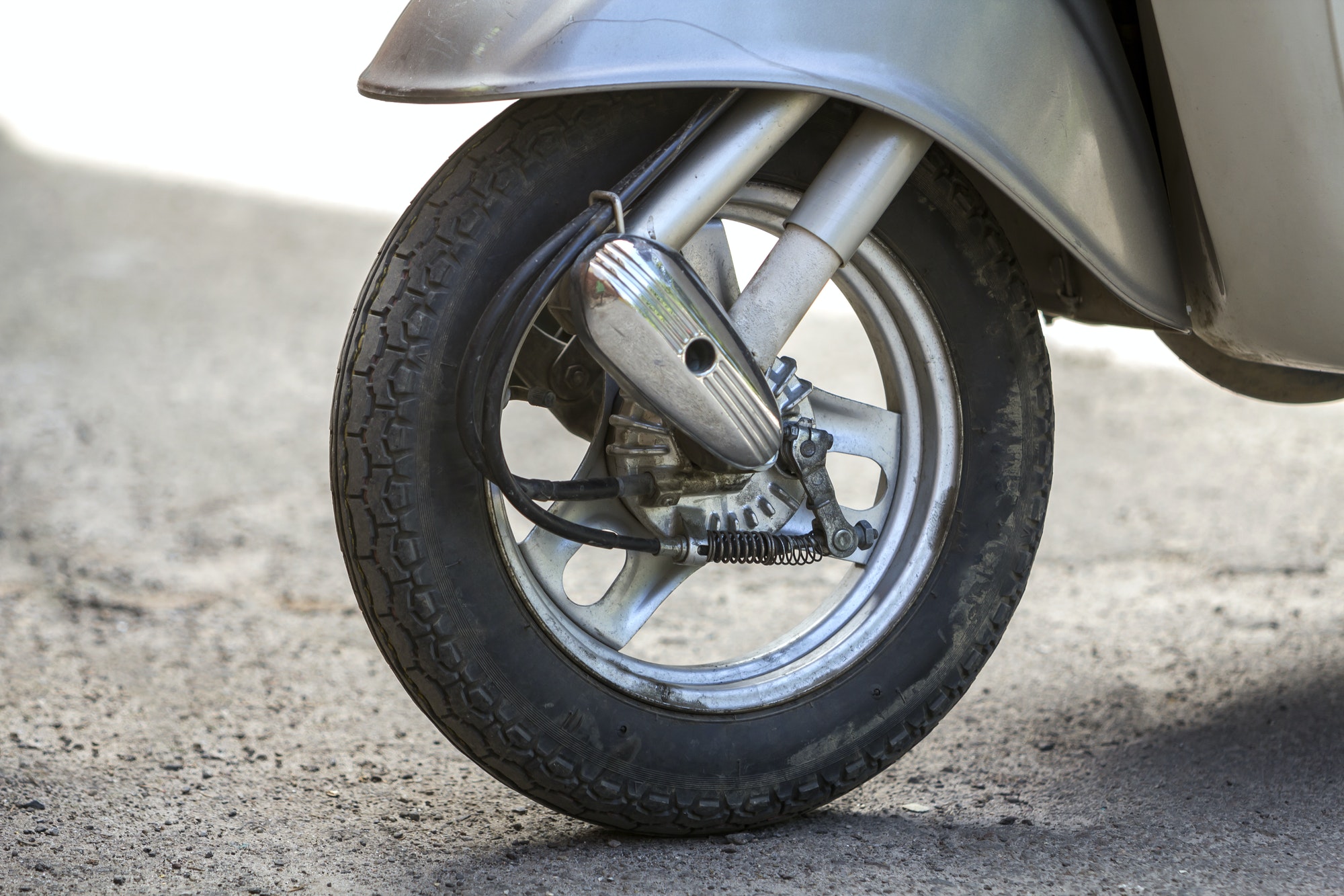 Close-up detail of new silver shiny motorbike scooter front wheel parked on blurred sunny background