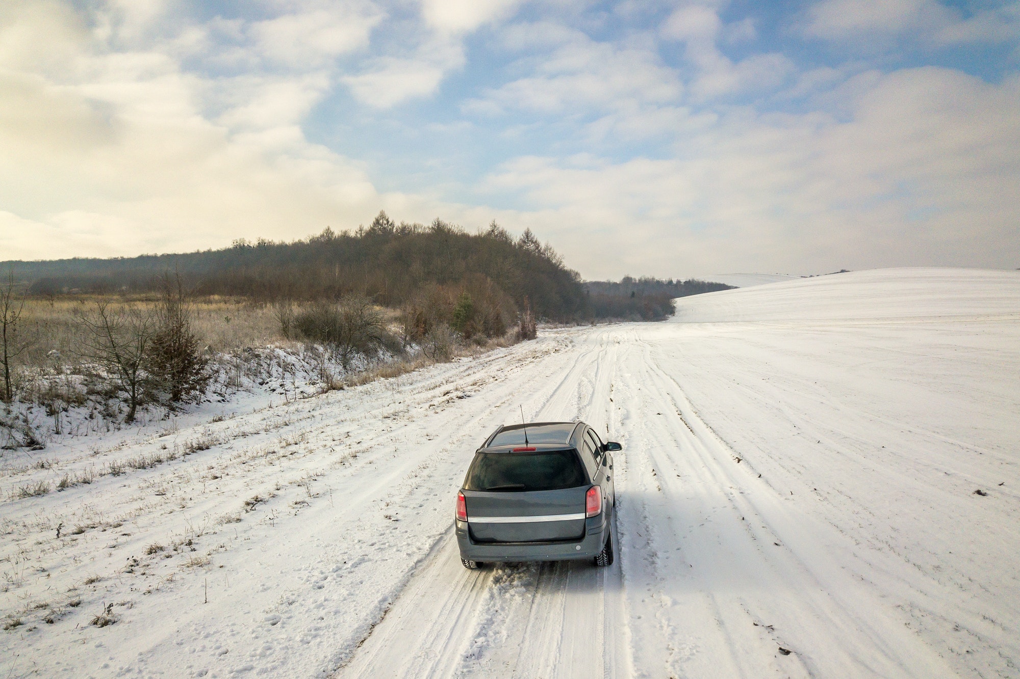 Family car driving on a dirt road in snow covered winter field