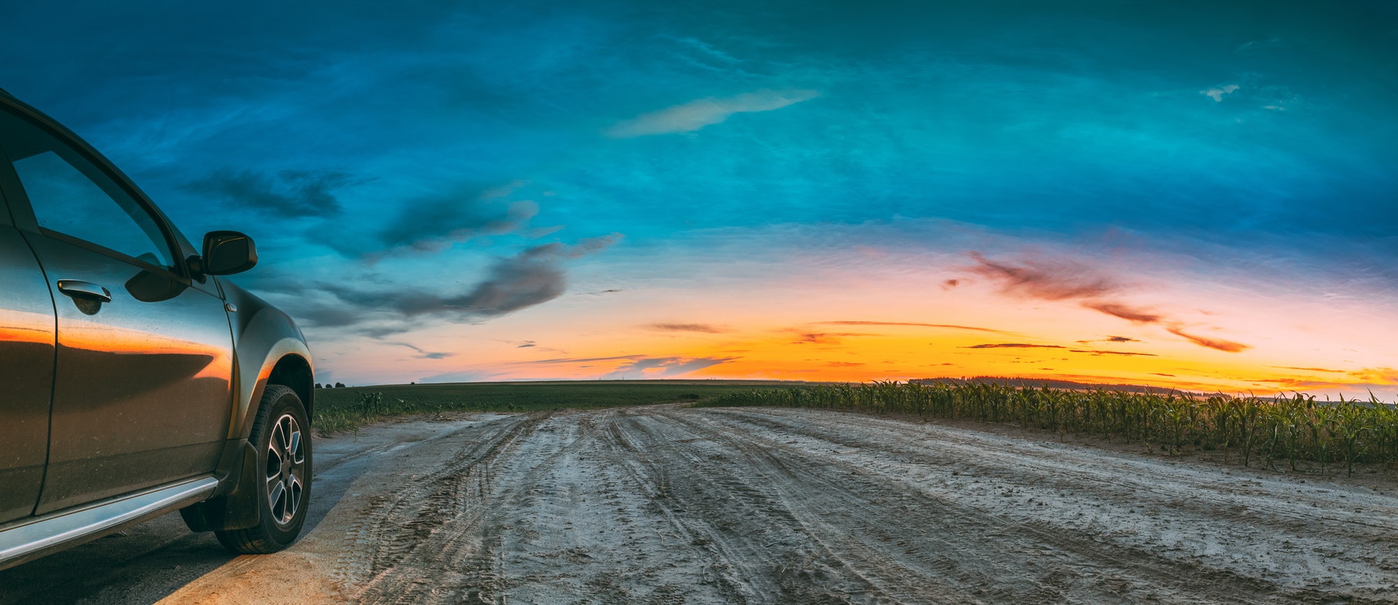 Green SUV Car Parked On Field Country Road Through Summer Maize Field In Amazing Sunset Time