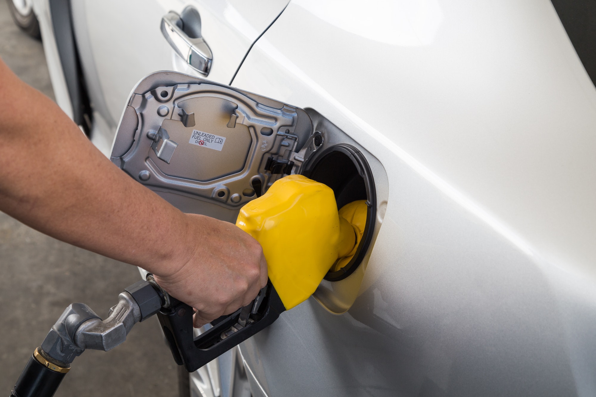 Hand with nozzle fueling unleaded gasoline into car