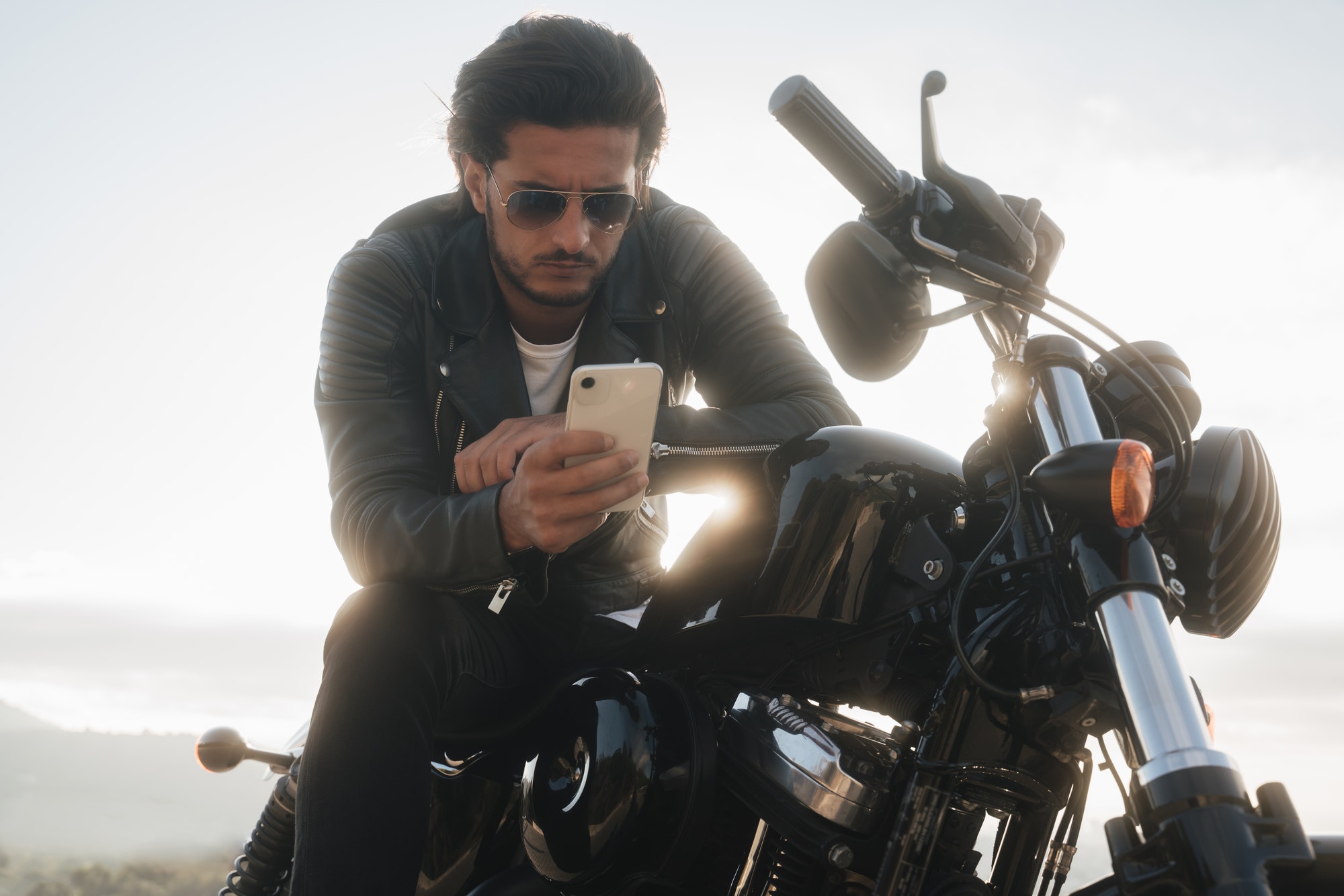 Handsome biker holding his smartphone, using navigation app to find the best road map