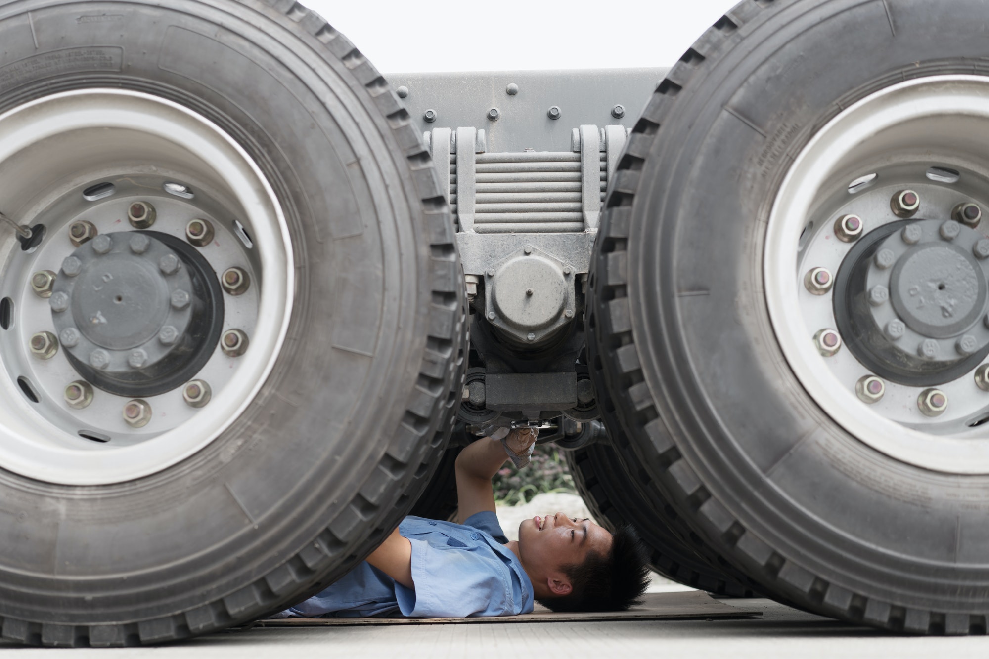 Male factory worker inspecting underneath truck in crane factory, China