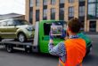 Male tow truck assistant photographing loaded car