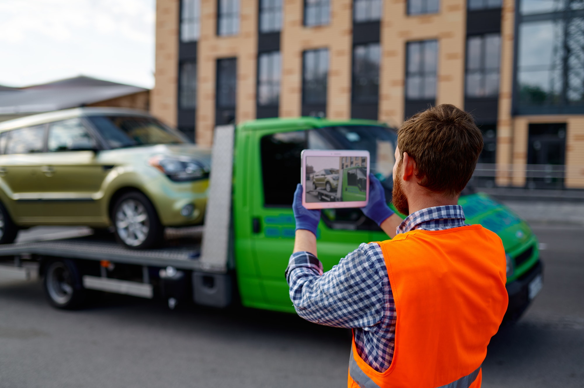 Male tow truck assistant photographing loaded car