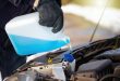 Man filling antifreeze coolant for cleaning front window with snow in background