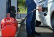 Man pumping gas into the gas tank of his vehicle car truck with gas cans lined up ready to be filled