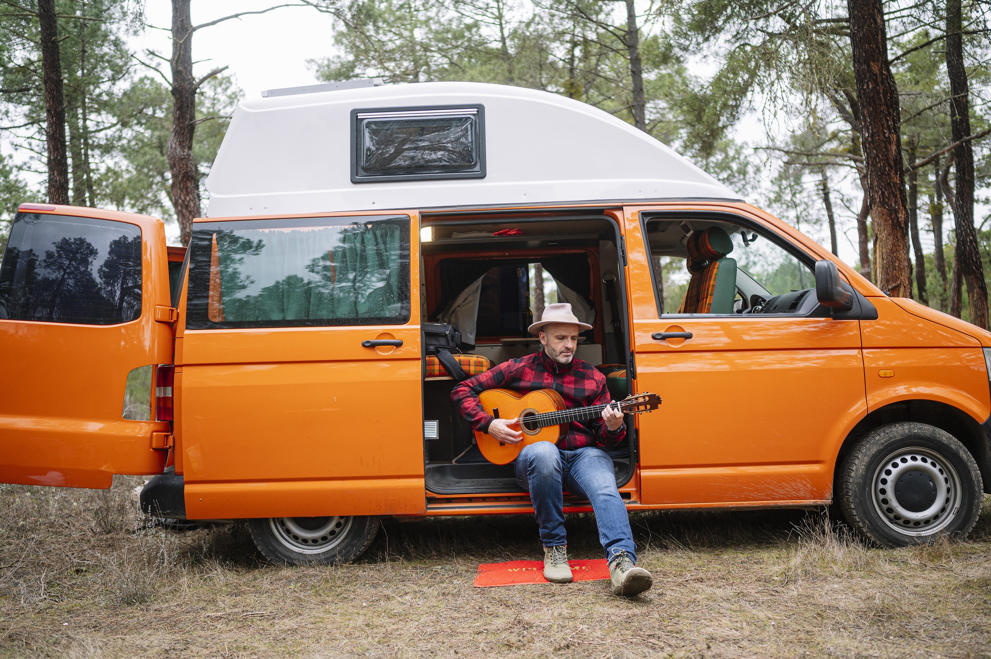 Man with hat playing guitar in a camper van.