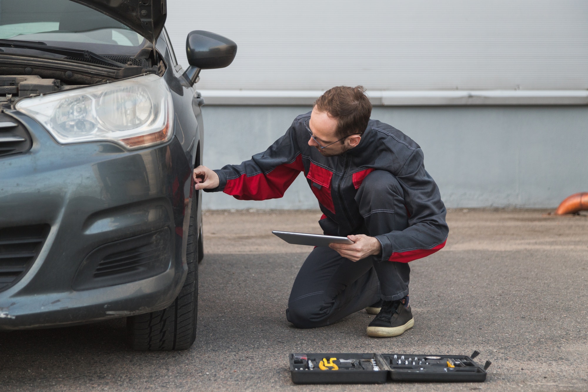 Mechanic with electronic tablet pc checking wheels and tires while working in the car repair center