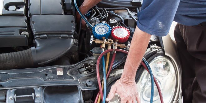 Mechanic with manometer inspecting auto vehicle air-condition co