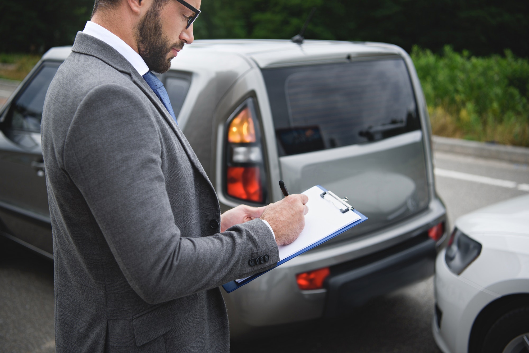 side view of man writing something to car insurance after car accident