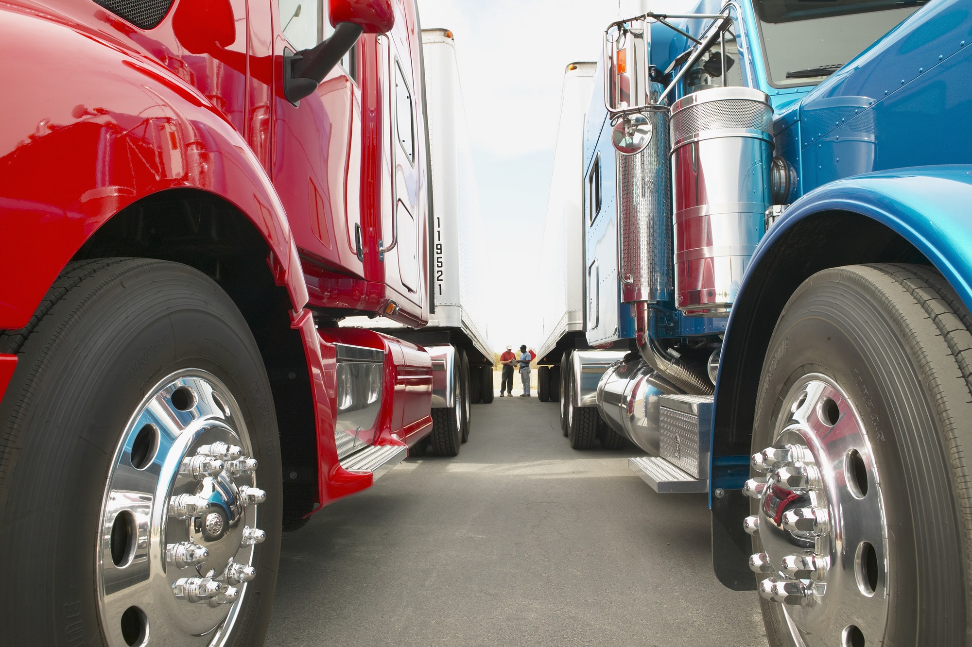 Truck drivers talking while standing between Class 8 trucks and trailers in a parking lot.