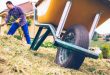 Wheelbarrow in the field and man raking on background