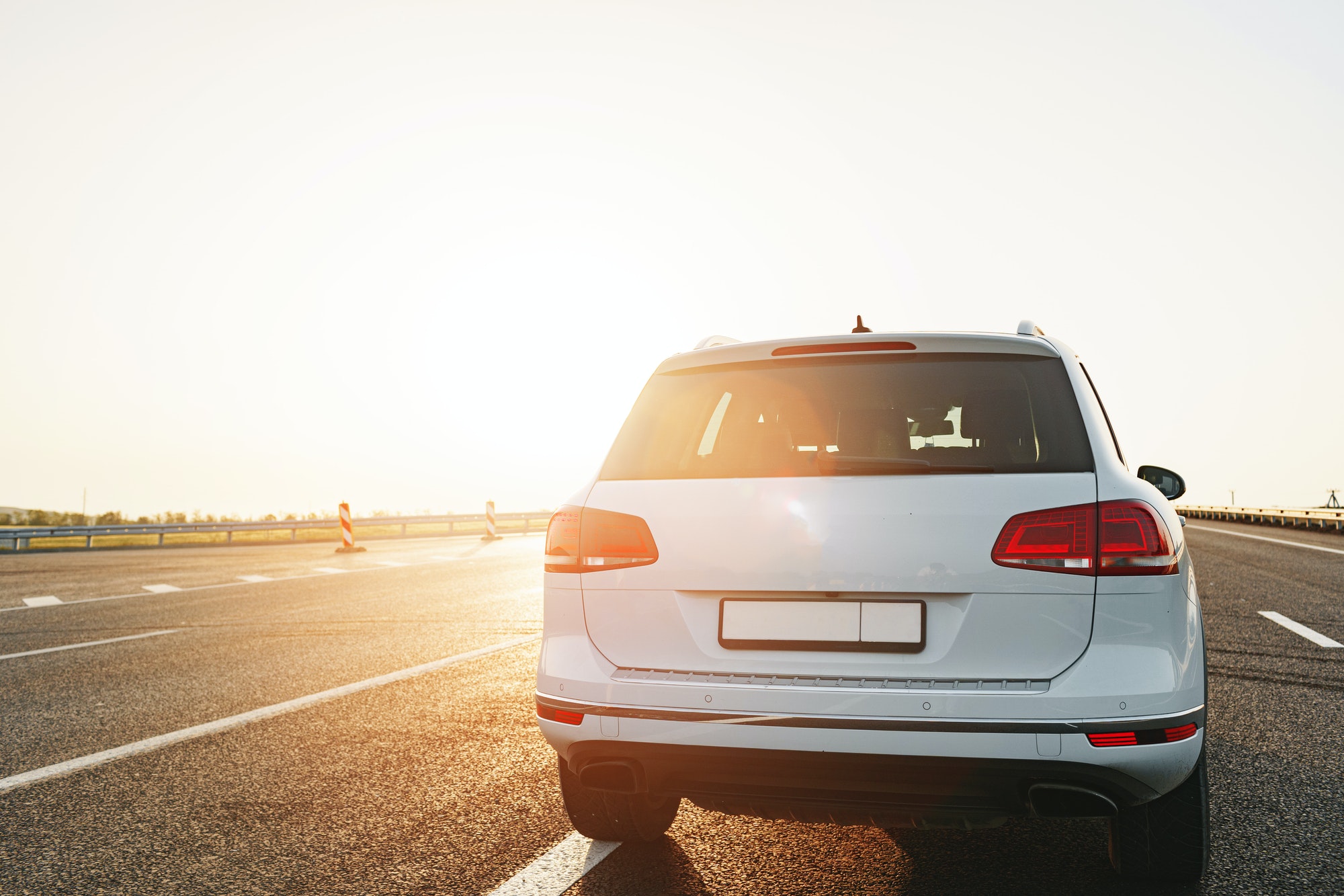 White crossover car on empty asphalt road at sunrise