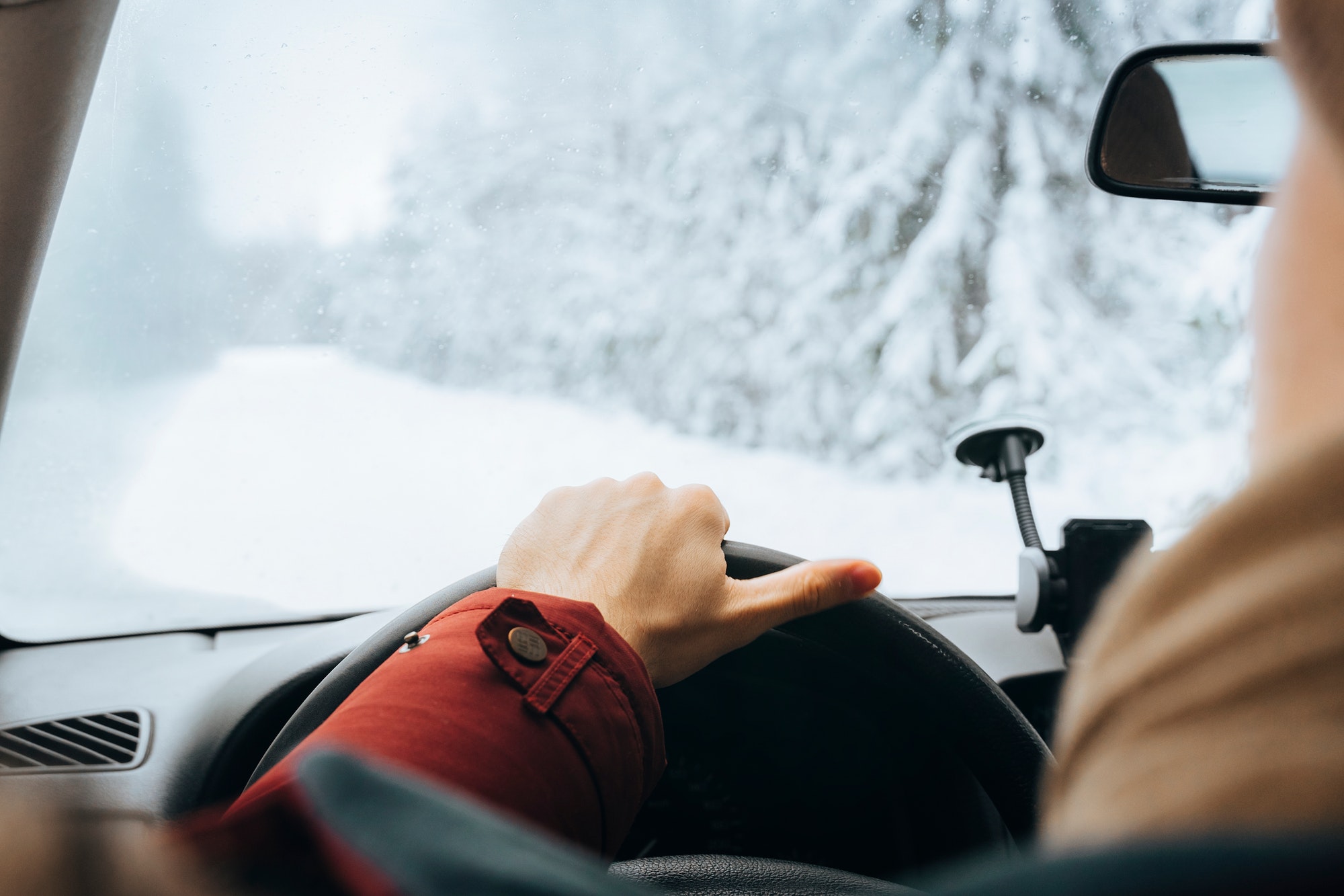 Winter road trip. Unrecognizable man driving car on snowy forest road. Hands on wheel