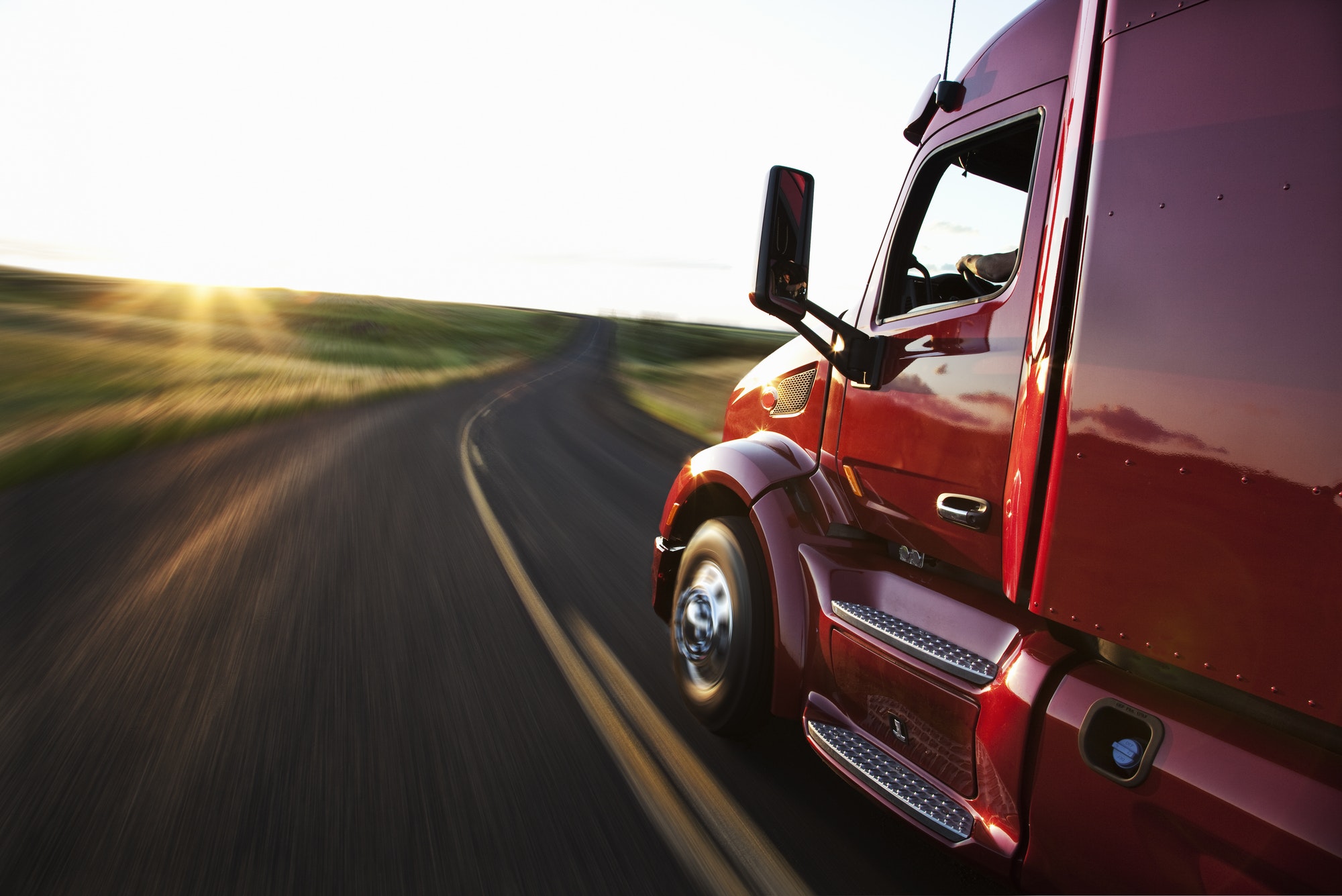 Close up side view looking forward of a commercial truck on a highway at sunset.