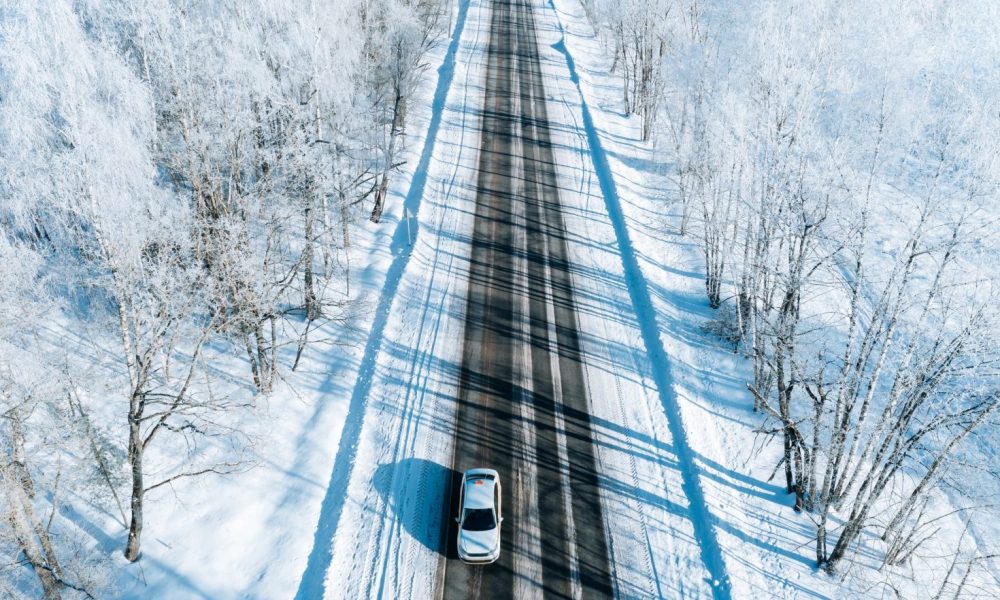 Aerial view of winter road with a car and snow covered trees.