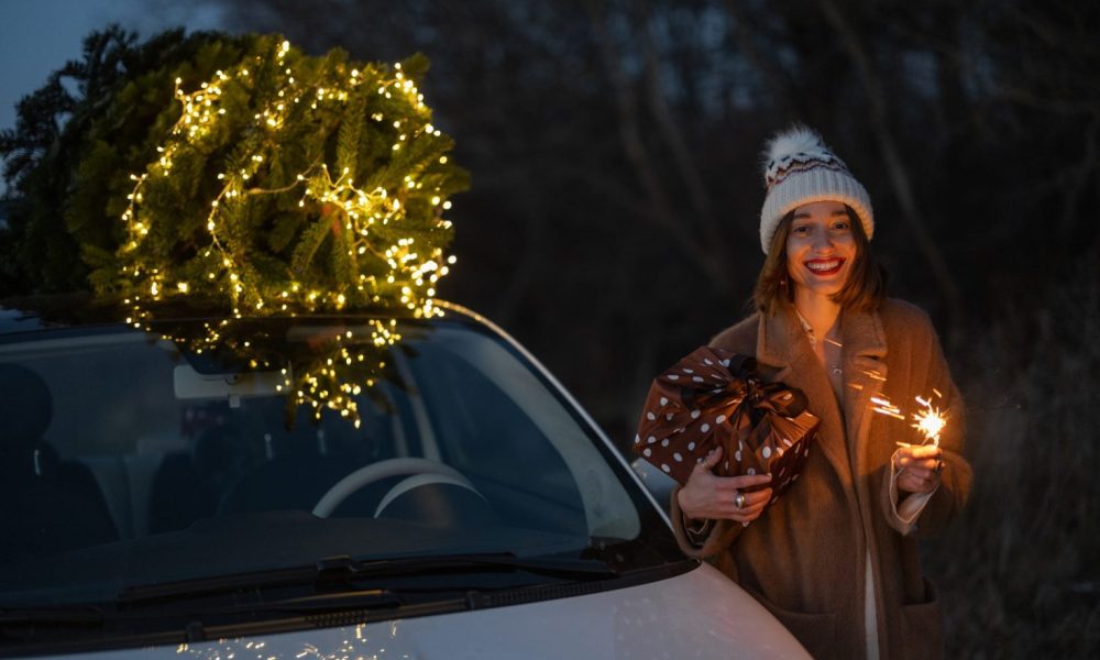 Woman with sprklers near car and Christmas tree outdoors