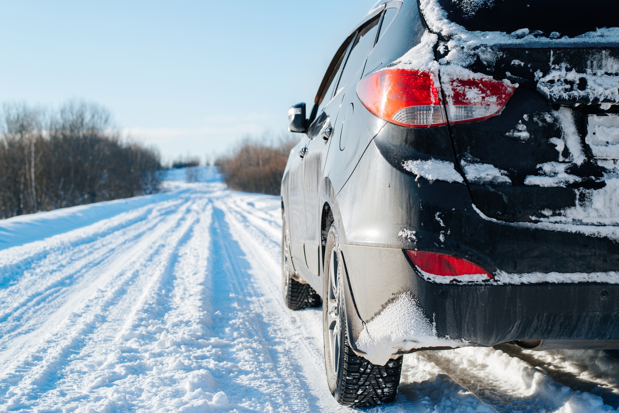 Black SUV car covered with snow standing on a snowy road on a sunny winter day, rear view