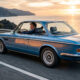 Coche clásico restaurado equipado con equivalencia neumáticos antiguos homologada, circulando por carretera costera con neumáticos modernos de estética vintage que mejoran seguridad, agarre y confort sin perder autenticidad.