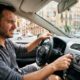Conductor incómodo en pleno verano dentro del coche intentando ajustar el aire acondicionado sin éxito.