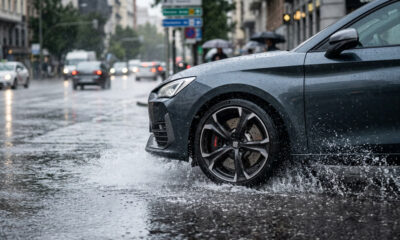 Ilustración realista de un coche reduciendo velocidad en asfalto mojado durante lluvia intensa, mostrando cómo los frenos mojados afectan la distancia de frenado y la seguridad.