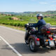 Un conductor viaja en un trike clásico tipo touring por una carretera secundaria rodeada de viñedos en La Rioja, mostrando la estabilidad y comodidad de este tipo de vehículo para trayectos largos.